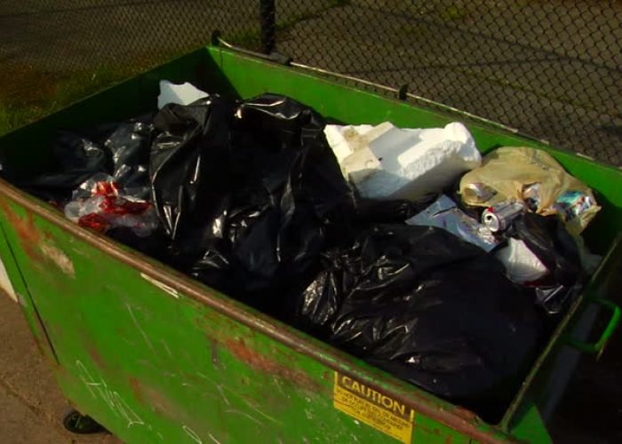a piece of trash is thrown into a green dumpster